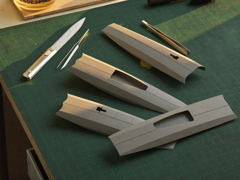 Stampate grigie di un kit di modellismo con taglierino e pinzette su tappetino verde